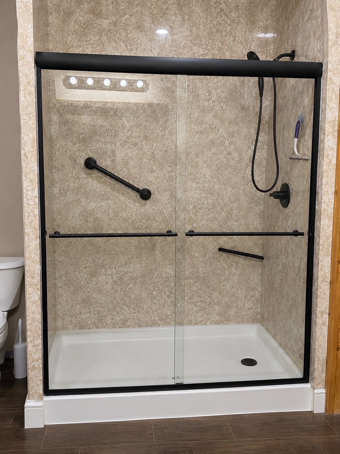 Walk-in shower with beige marble-look walls, grab bar and handheld shower