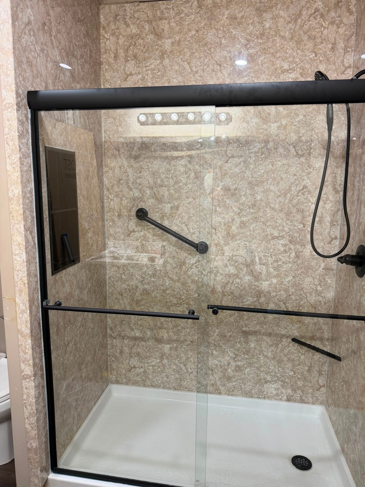 Walk-in shower with beige surround, glass doors and handheld shower
