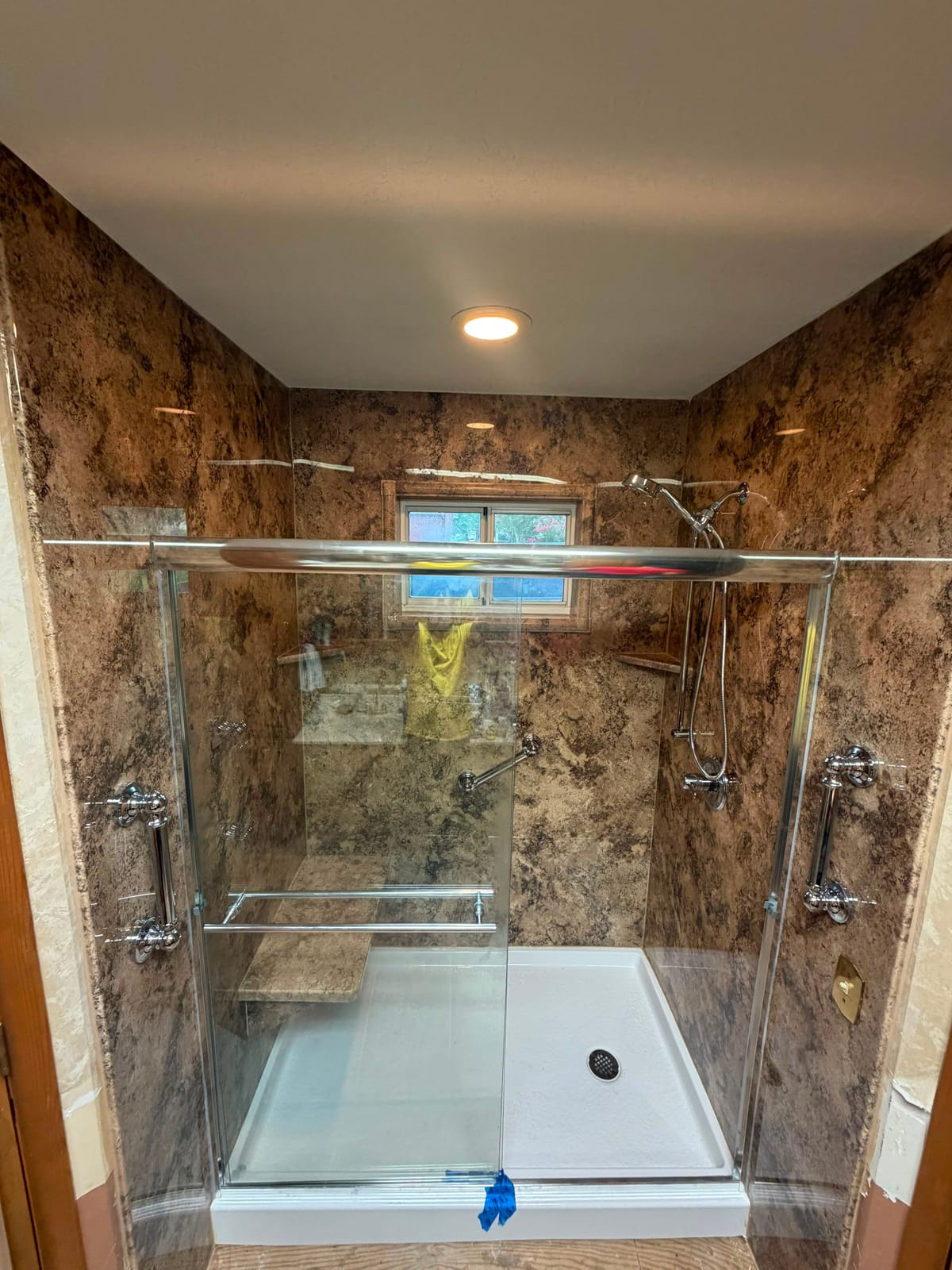 Walk-in shower with brown marble-look walls, bench seat and glass doors
