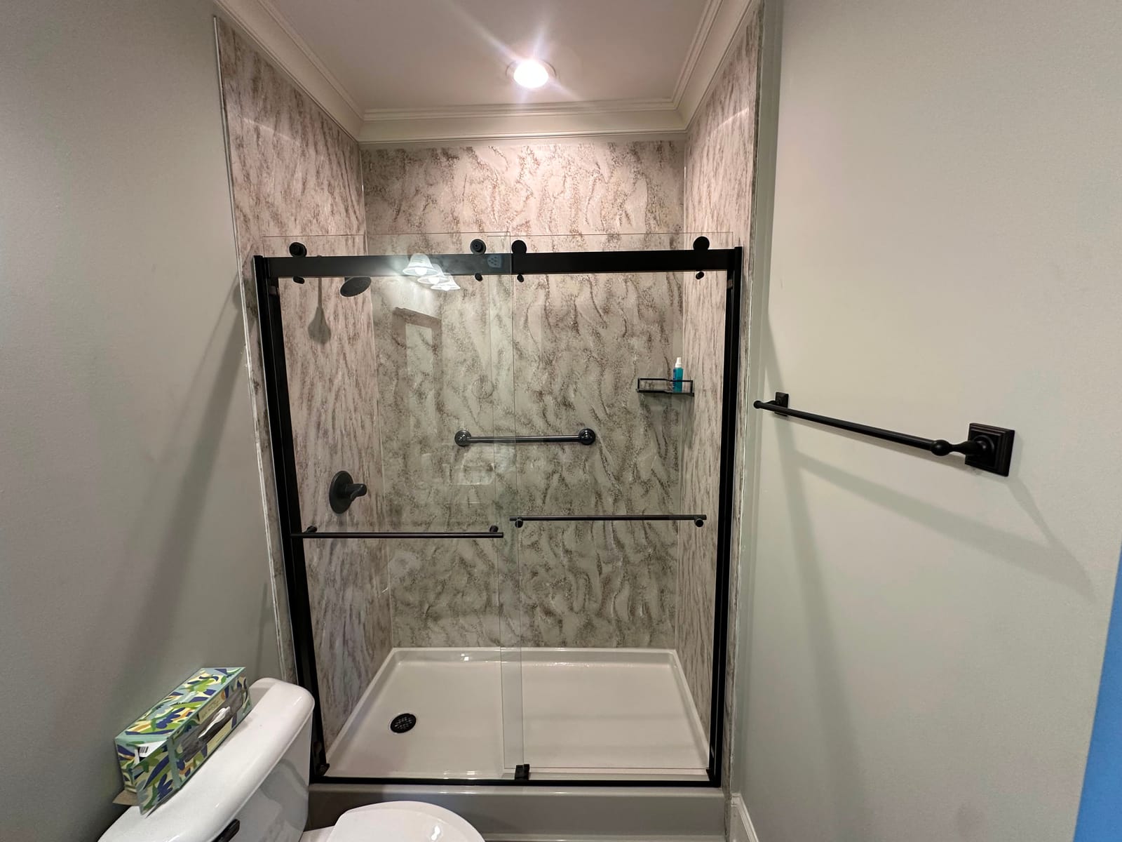 Walk-in shower with marble-look walls, glass doors and black fixtures