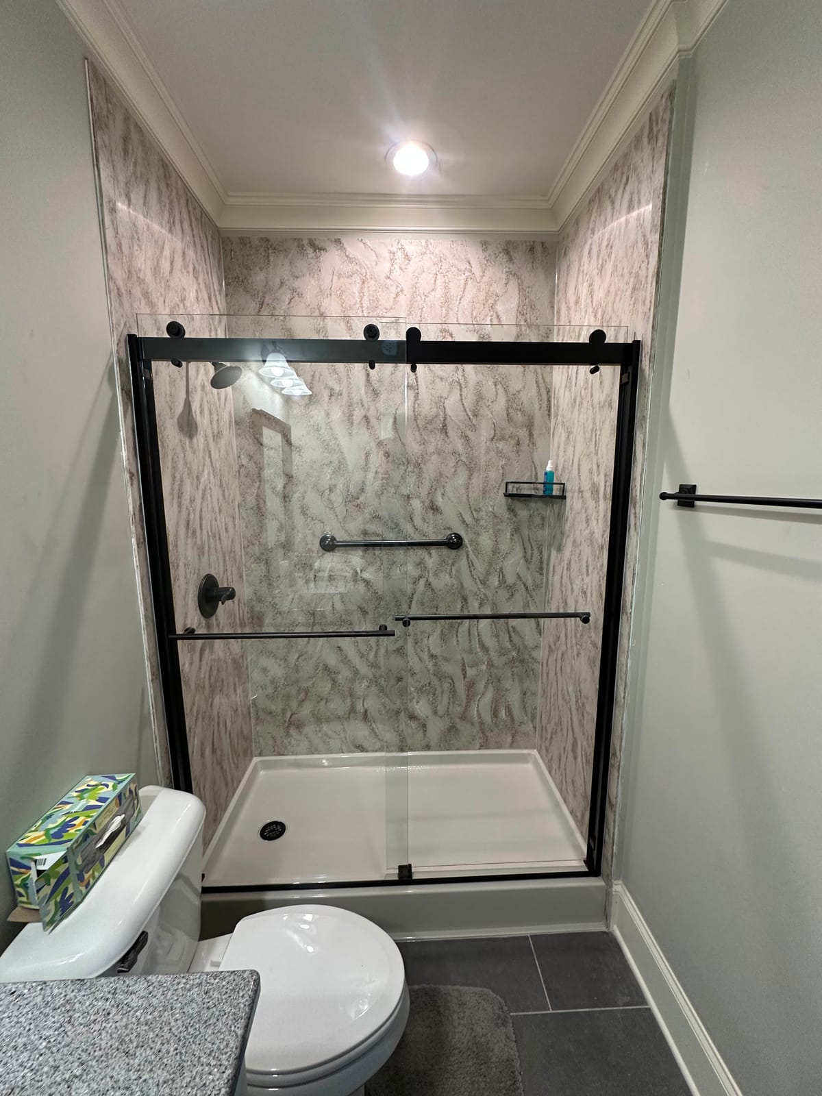 Walk-in shower with marble-look surround and black-framed glass doors