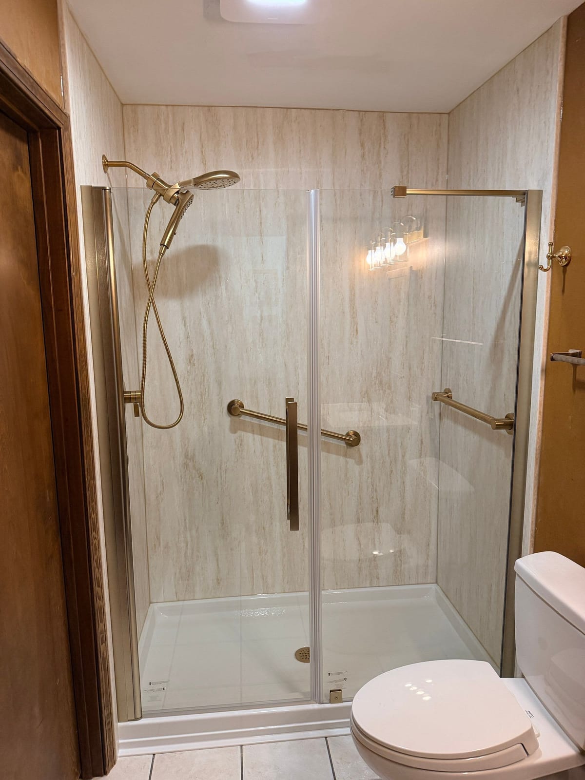 Walk-in shower with travertine-look surround and champagne bronze fixtures